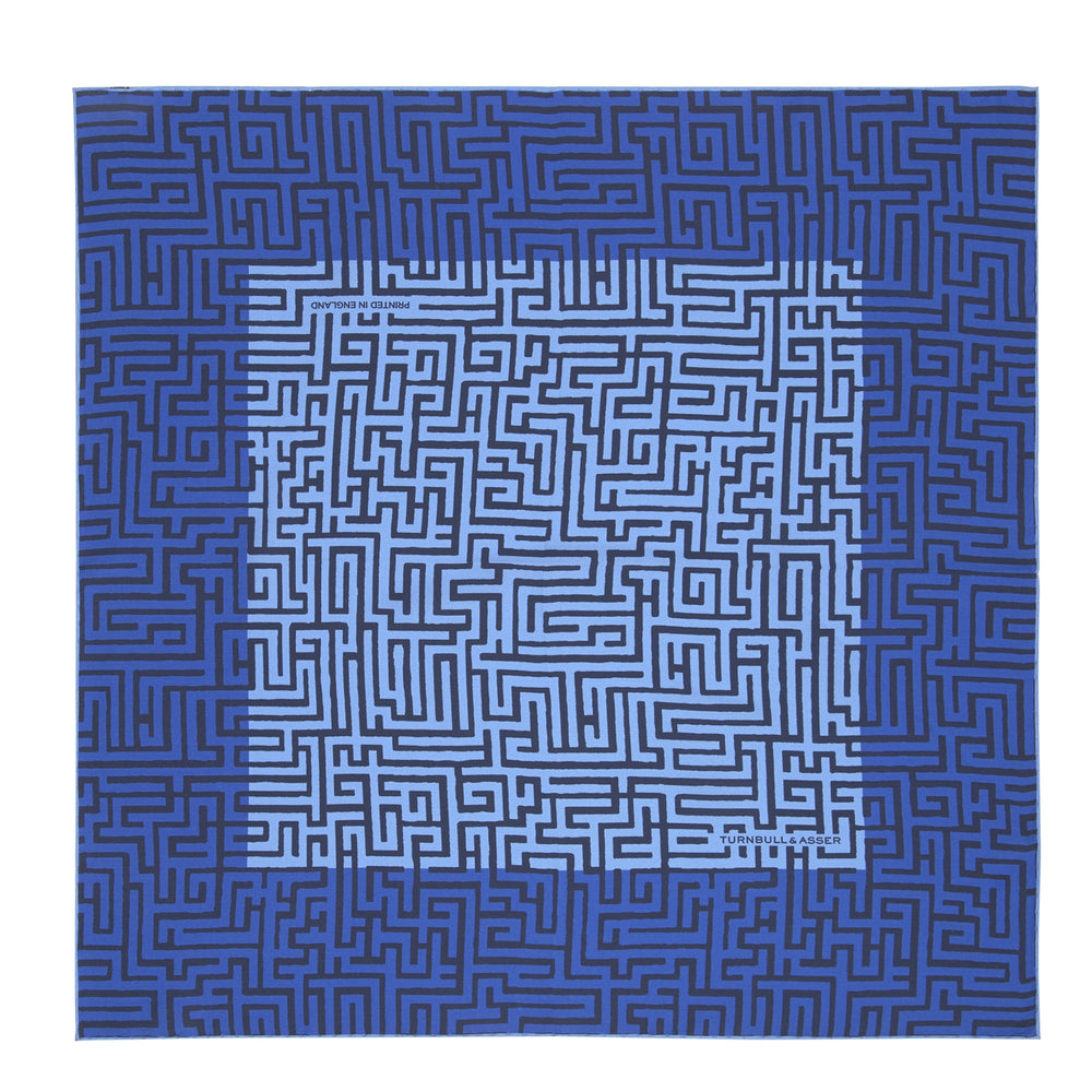 The Blue Maze Silk Pocket Square by Turnbull & Asser features a geometric maze-inspired pattern and central logo, with a folded corner for an artful touch.
