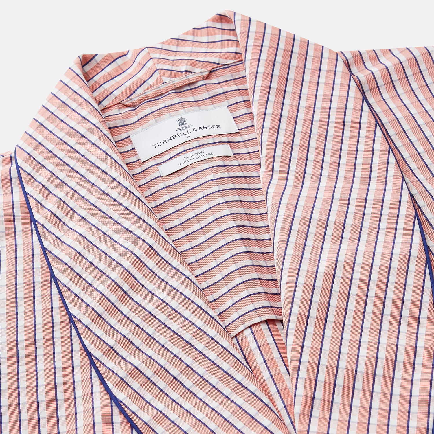 View 3 of product The Turnbull & Asser Orange Multi Check Cotton Arnold Gown features long sleeves, a shawl collar, wrap-around belt, and dark piping on the edges and pocket, displayed flat on a white background.