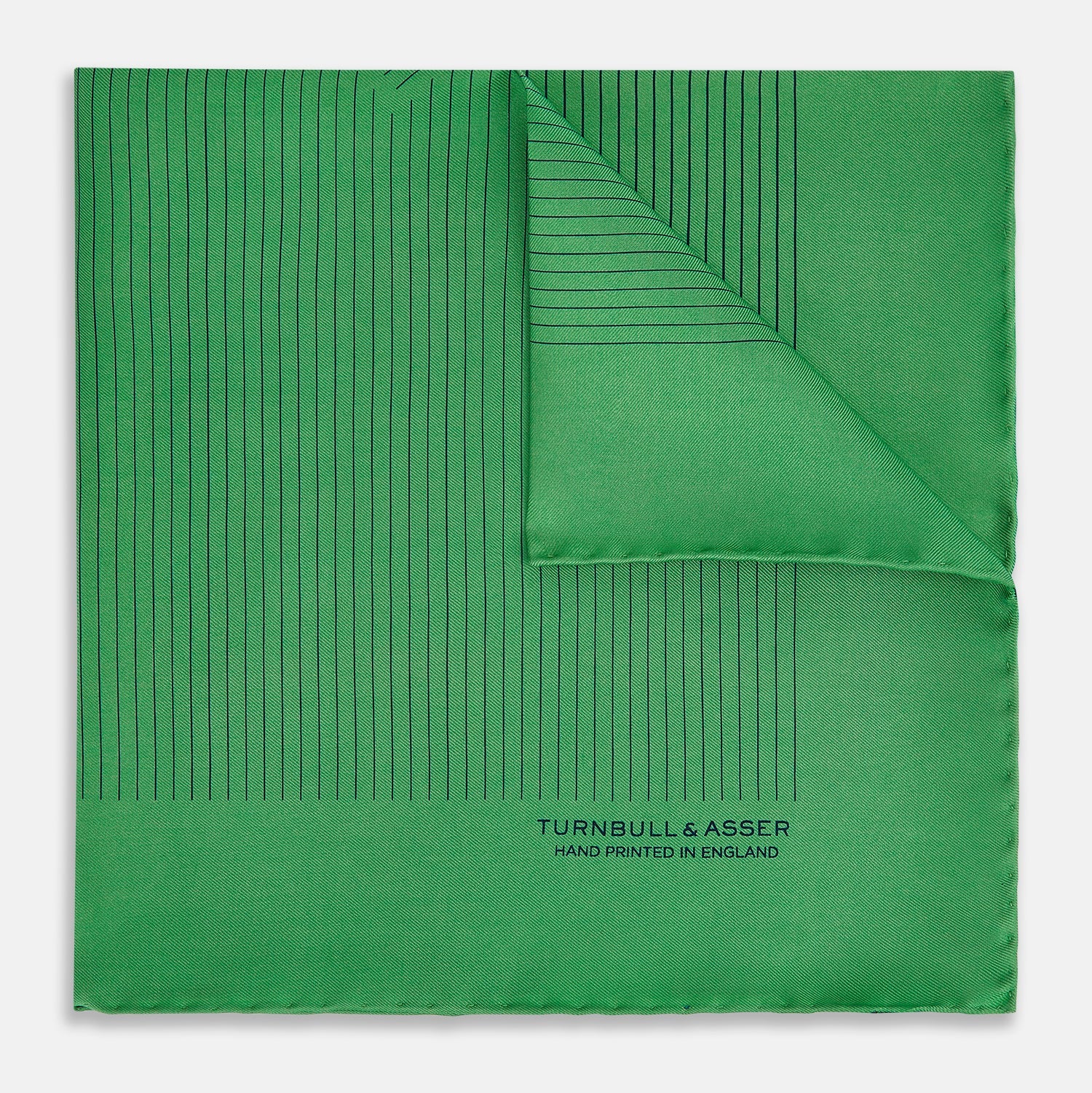 View 1 of product The Hunter Green Stripe Silk Pocket Square by Turnbull & Asser features thin black vertical stripes on one corner and “Turnbull & Asser Hand Printed in England” printed in black, reflecting classic British heritage.