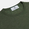 View 4 of product A man stands facing the camera against a plain light background, wearing the Turnbull & Asser Bottle Green Merino Kingston Crew Neck Jumper with dark pants and black shoes. His arms rest at his sides and he has a neutral expression.