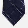View 4 of product The Turnbull & Asser WINDOW PANE NAVY RIVER TIE features a navy blue base with a subtle light blue check pattern, elegantly rolled on a white background—a sophisticated men's accessory for any wardrobe.