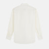 View 6 of product A man in a Cream Silk Regular Fit Ruffle-Front Wilfred Shirt by Turnbull & Asser stands against a dark background, one hand on a chair, gazing thoughtfully to the side.