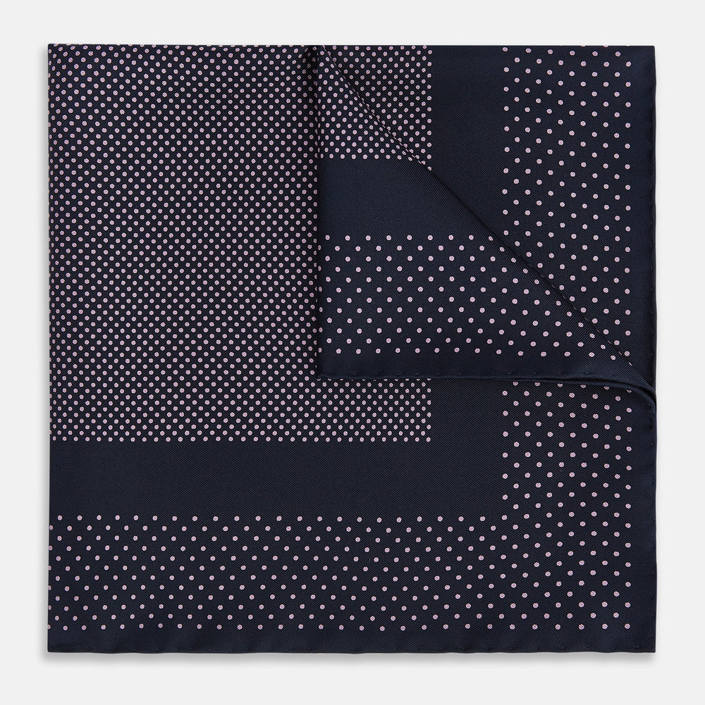 The Turnbull & Asser Navy and Lilac Dot Silk Pocket Square features small white polka dots with a wider border of spaced-out dots, neatly folded to showcase both sides of its handmade silk fabric.
