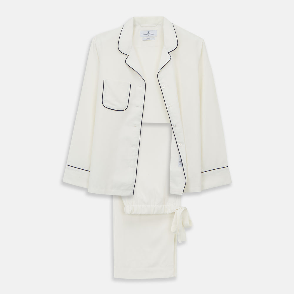 The Women's Harriet Cream Silk Pyjama Set by Turnbull & Asser features a white sand-washed silk button-up top with black piping and chest pocket, plus matching drawstring pants, all shown against a white background.