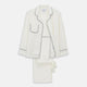The Women's Harriet Cream Silk Pyjama Set by Turnbull & Asser features a white sand-washed silk button-up top with black piping and chest pocket, plus matching drawstring pants, all shown against a white background.