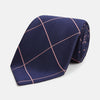 View 1 of product The Turnbull & Asser FONDANT PINK and WINDOW PANE NAVY Silk Tie features a subtle ribbed texture with a pink grid pattern on navy—an elegant choice for polished office attire, shown neatly rolled on a white background.