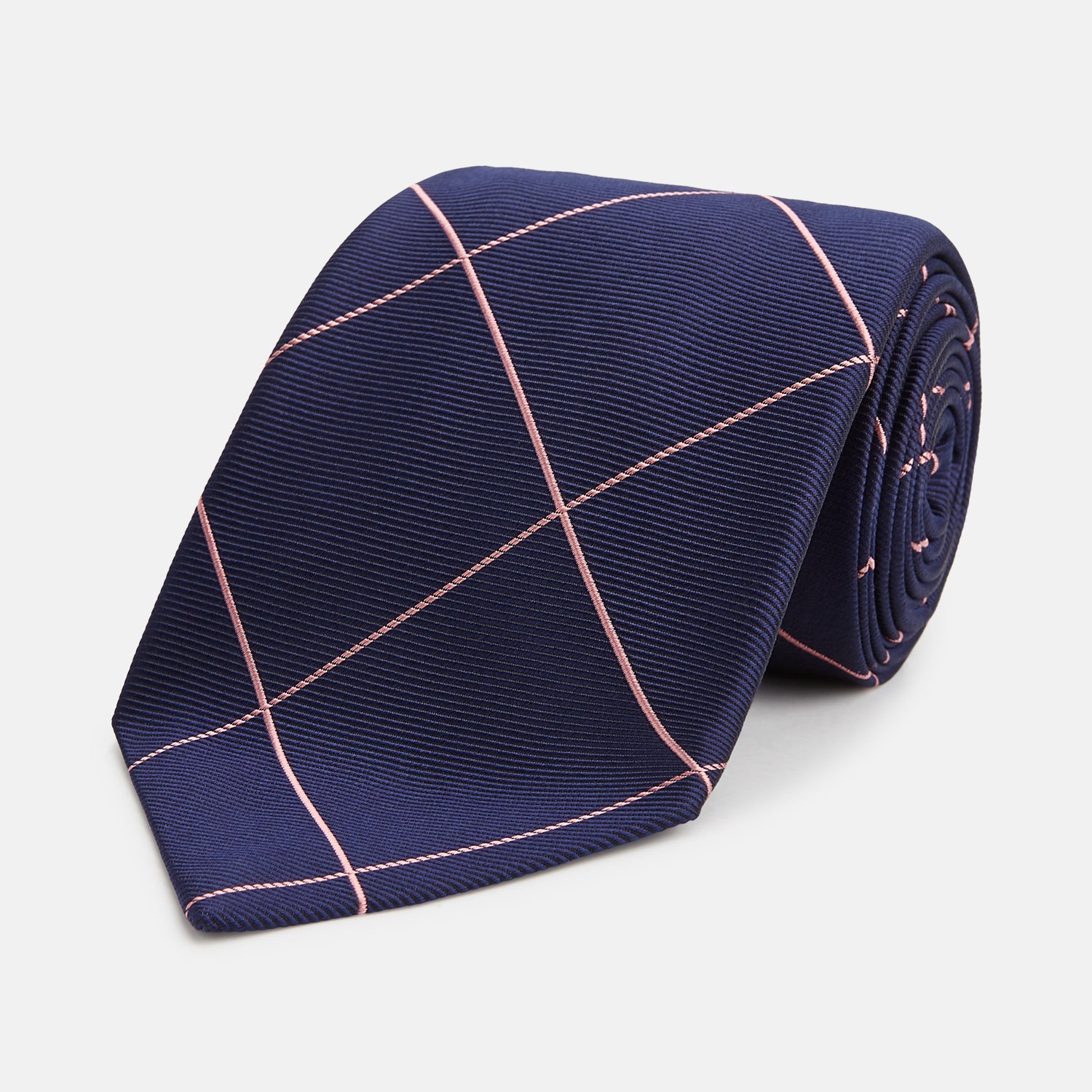 View 1 of product The Turnbull & Asser FONDANT PINK and WINDOW PANE NAVY Silk Tie features a subtle ribbed texture with a pink grid pattern on navy—an elegant choice for polished office attire, shown neatly rolled on a white background.