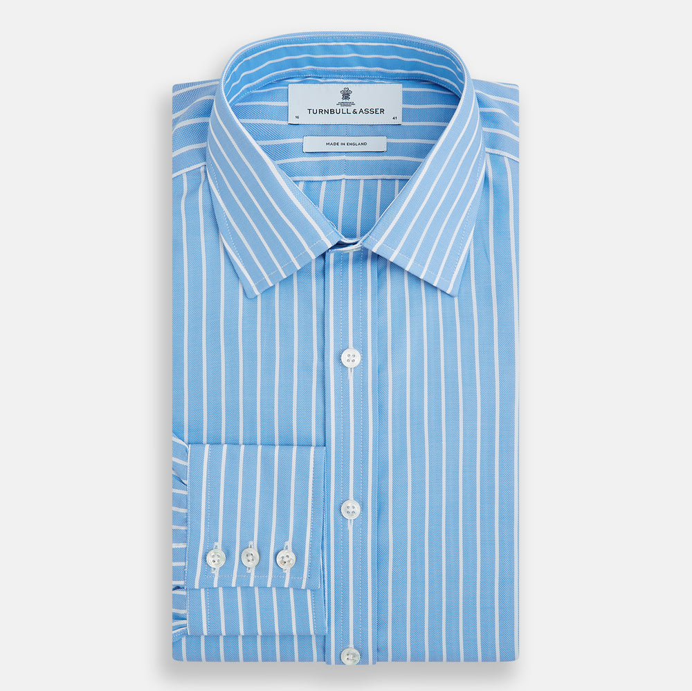 The Turnbull & Asser Sky Blue Wide Pinstripe Mayfair Shirt features long sleeves, a classic collar, and buttoned cuffs, laid flat against a white background for a refined formal look.