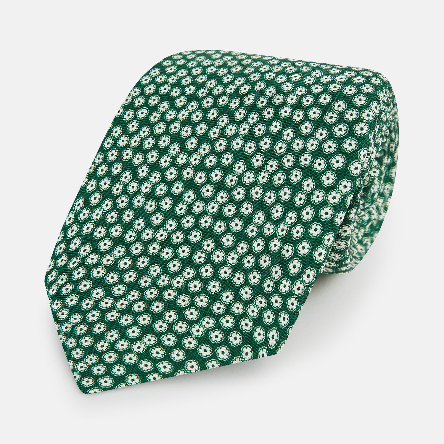 View 1 of product The Forest Green Flower Patterned Silk Tie by Turnbull & Asser features a white floral motif on silk, shown neatly rolled against a plain white background.