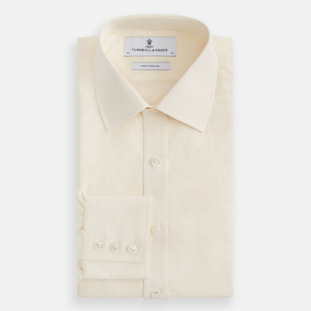 The Cream Fine Pencil Stripe Mayfair Shirt by Turnbull & Asser features long sleeves, a pointed collar, and buttoned cuffs. Crafted from breathable cotton with fine pencil stripes, it is shown laid flat on a white background.
