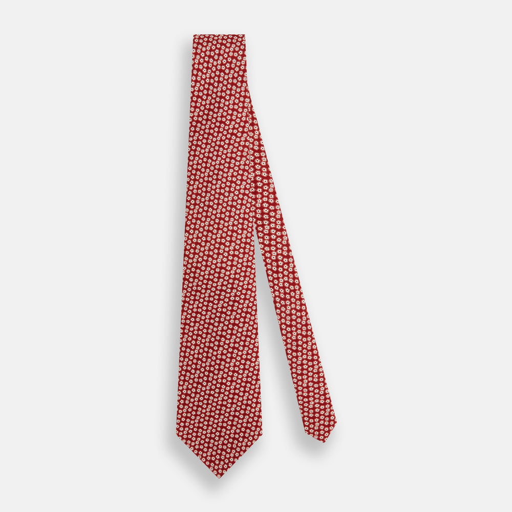 The Red Flower Patterned Silk Tie by Turnbull & Asser, crafted from fine English silk, features a delicate white floral design and is neatly rolled on a white background.