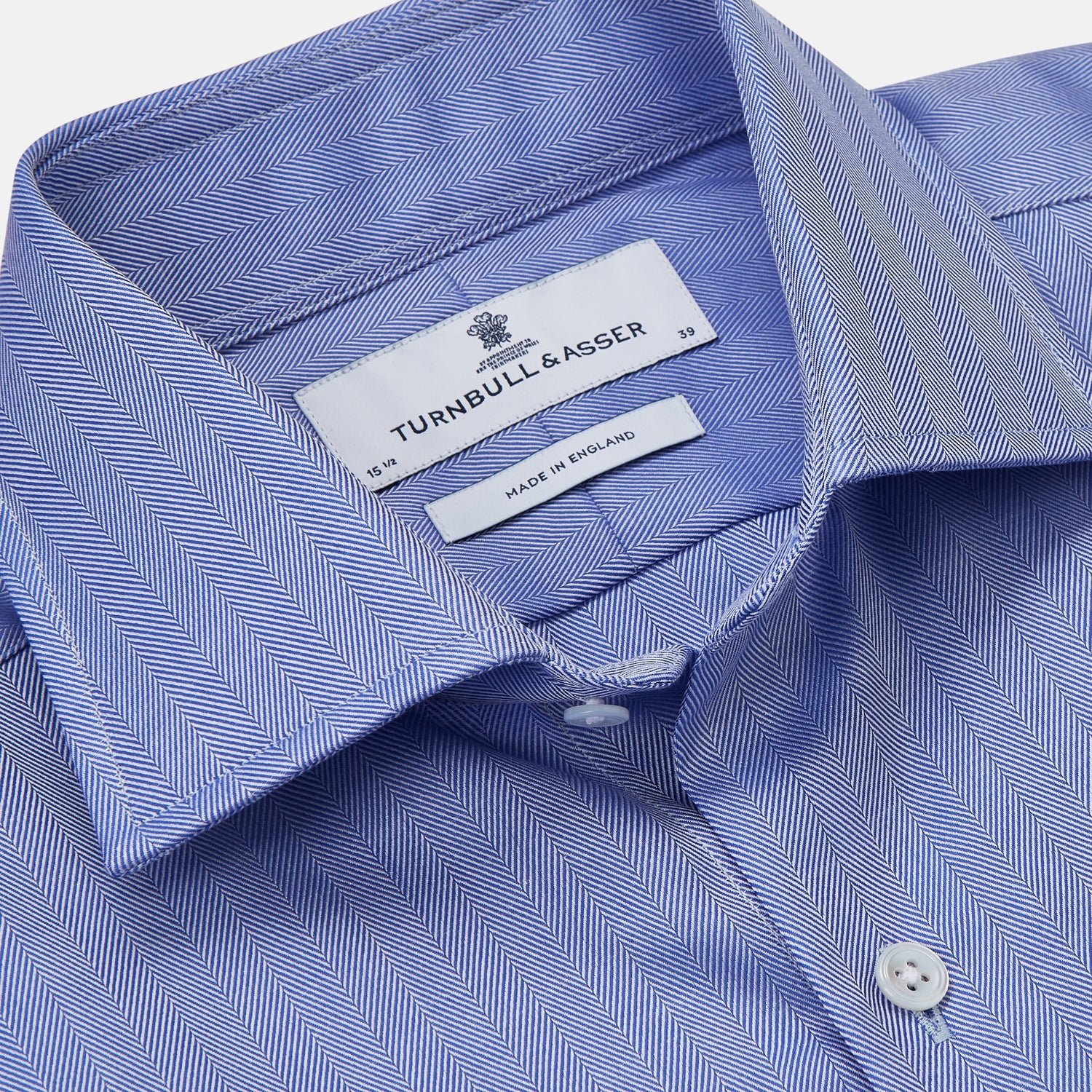 View 5 of product Turnbull & Asser's Blue Herringbone Tailored Fit Shirt with a Kent collar and white buttons is shown laid flat on a white background.