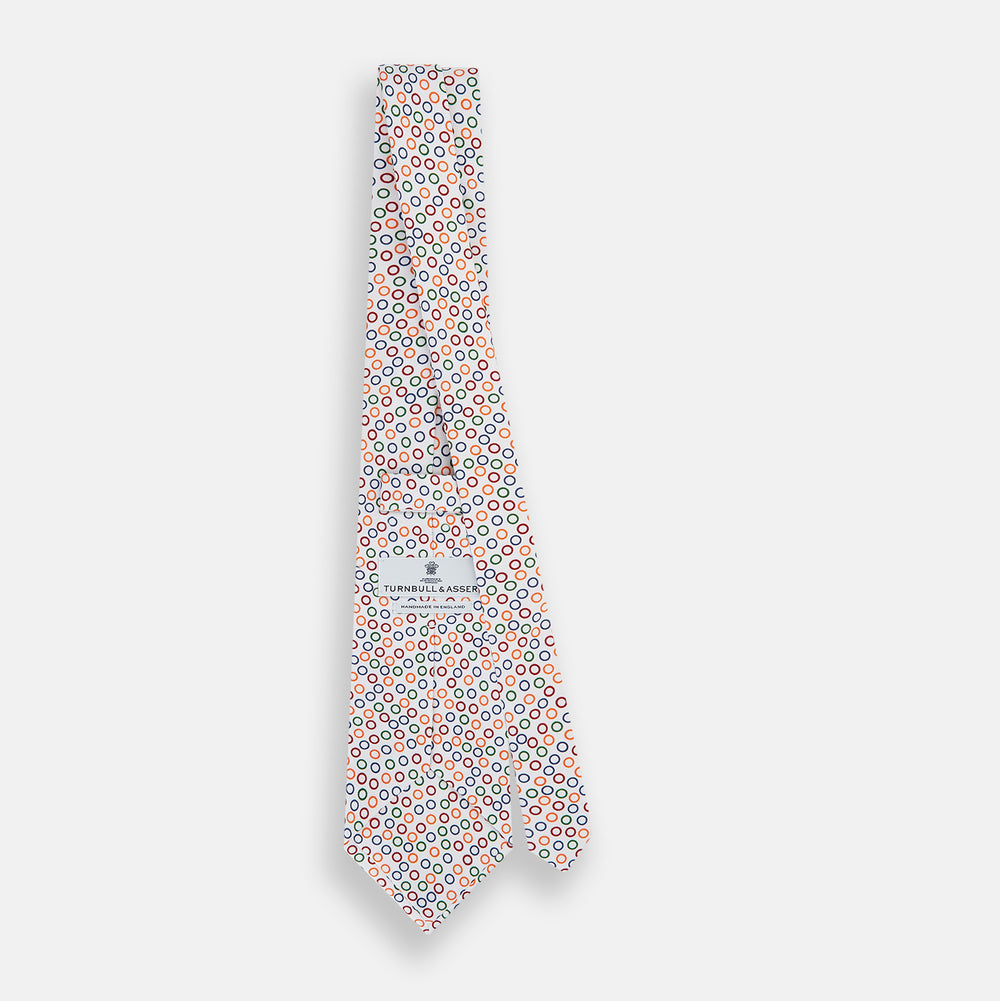 The Turnbull & Asser Confetti Circle White Silk Tie features colorful rings in red, orange, blue, and green scattered across a crisp white background.