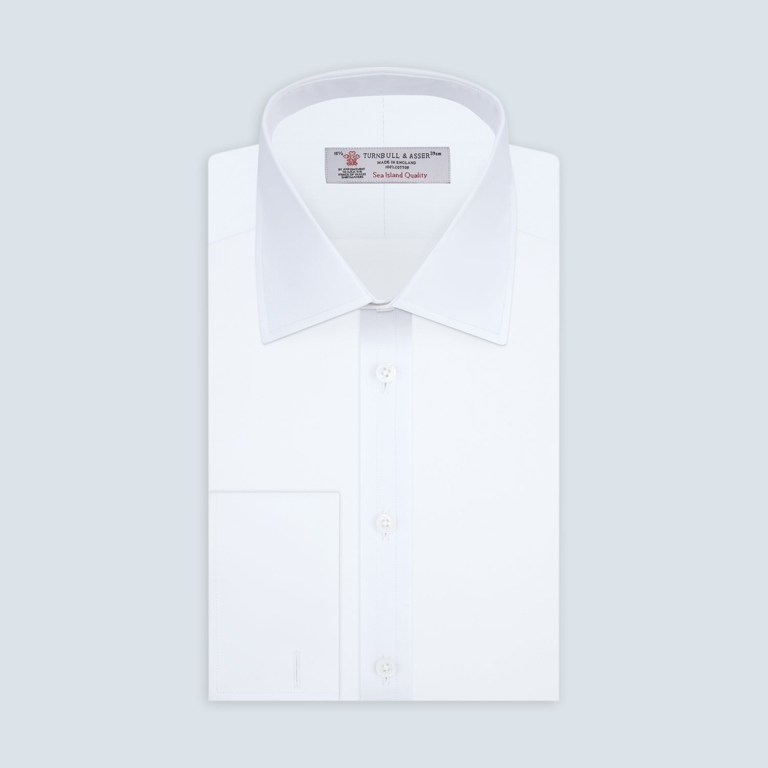 View 1 of product A neatly folded White Sea Island Quality Cotton Twill Shirt by Turnbull & Asser, featuring a T&A collar and 3-button cuffs, is displayed on a light grey background with a label visible inside the collar.