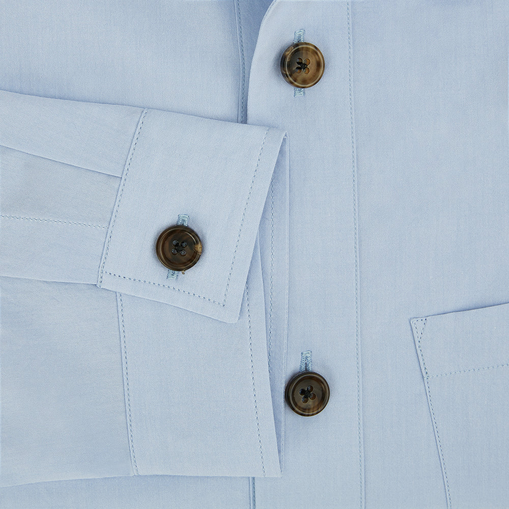 The Turnbull & Asser Pale Blue Hyde Overshirt is a long-sleeve, sanforised cotton button-up with a single chest pocket and dark buttons, shown on a plain white background.