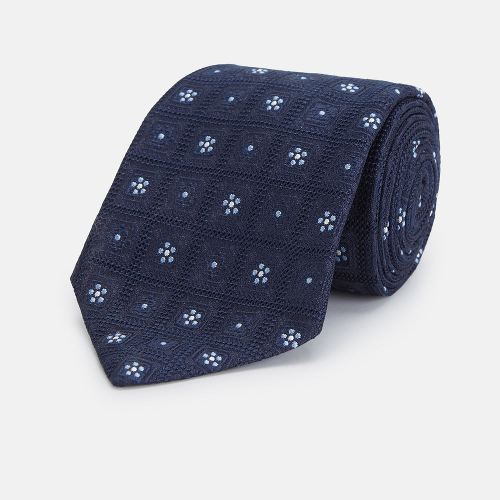 The Turnbull & Asser Jacquard Silk Circle Tie showcases a textured navy blue design with small white and light blue floral motifs—an essential accessory for refined attire.