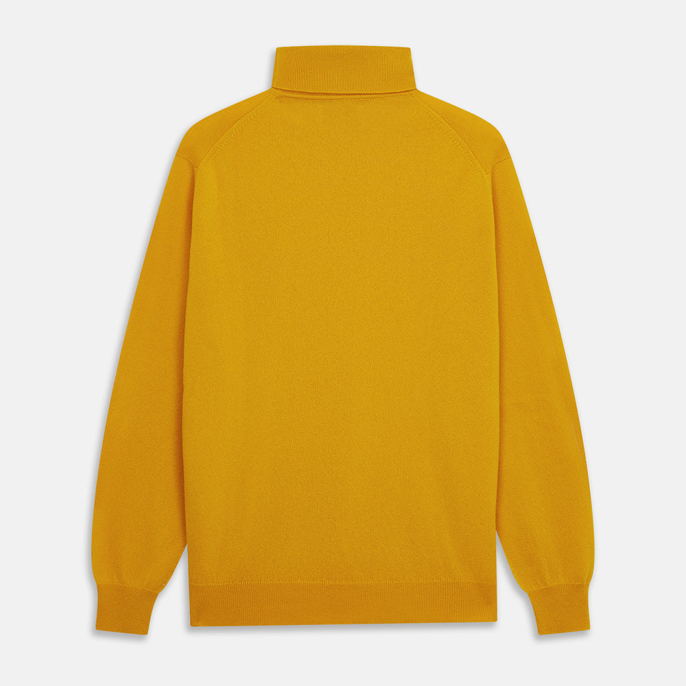 A man with short hair and a beard wears the Gold Aubrey Cashmere Roll Neck Jumper by Turnbull & Asser with dark pants, standing against a plain beige background and calmly looking at the camera, highlighting this stylish autumn sweater look.