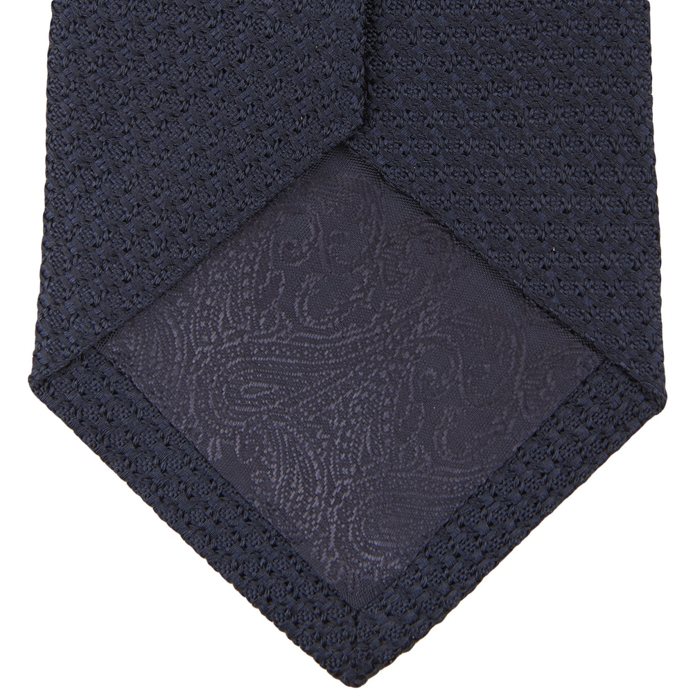 The Turnbull & Asser Plain Woven Grenadine Silk Tie in navy, with a textured finish, is rolled and displayed on a white background—a refined essential for any wardrobe.