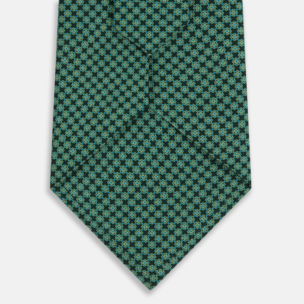 The Turnbull & Asser Forest Green Geometric Floral Silk Tie, showcasing a subtle green and dark blue pattern, is neatly rolled and set against a plain white background.