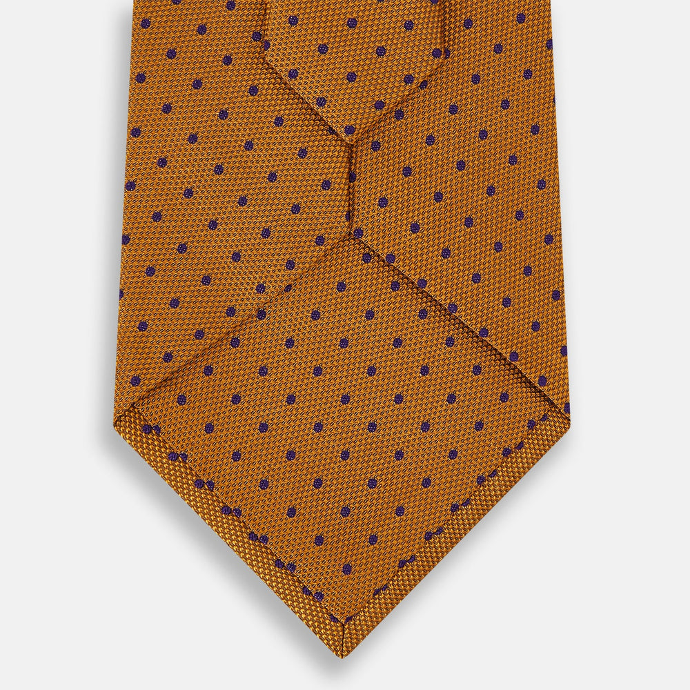 The Turnbull & Asser Purple and Orange Micro Dot Silk Tie features a pattern of small blue dots, shown rolled up on a white background.