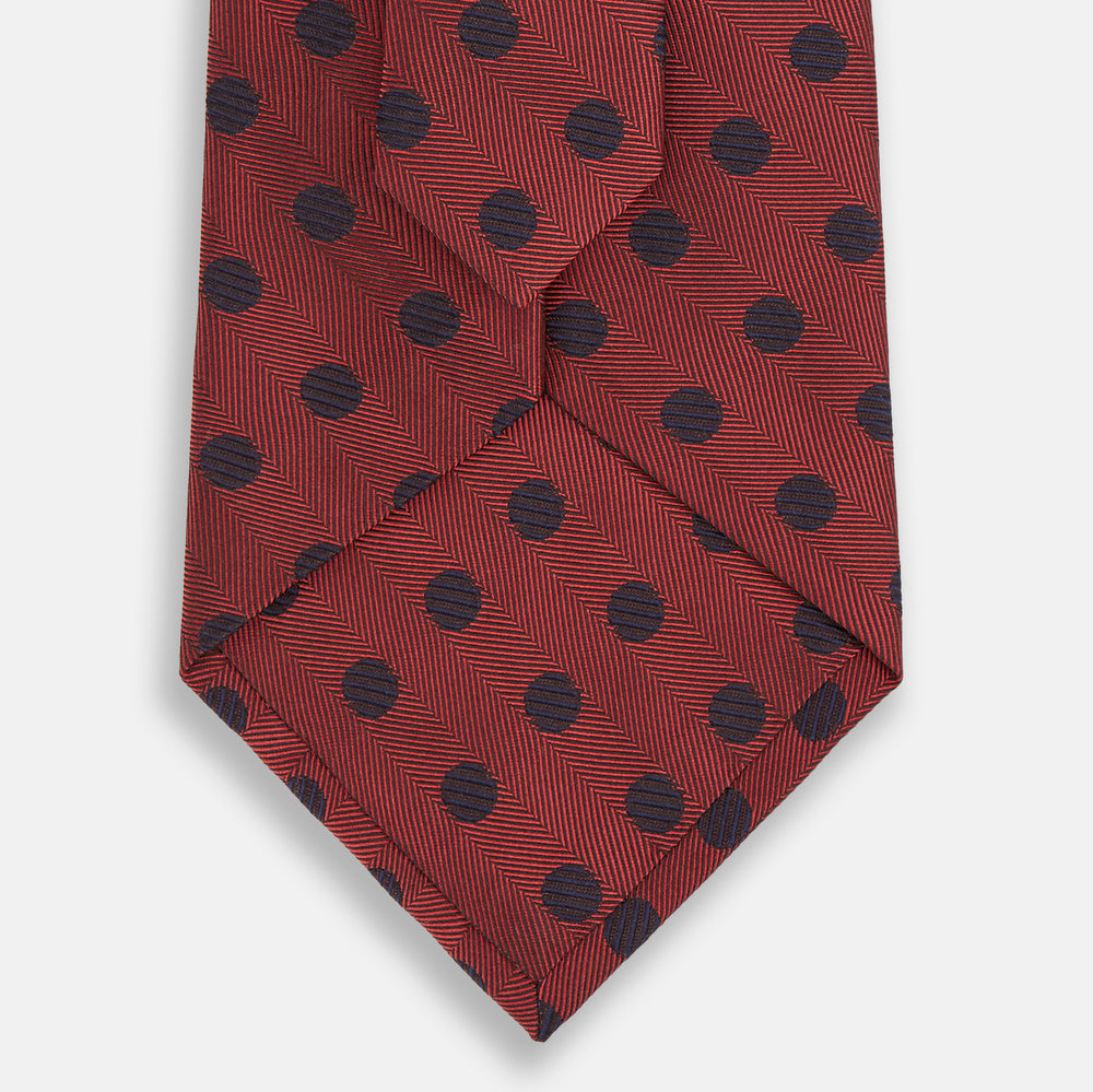 A Turnbull & Asser Navy Dot and Red Silk Tie, featuring a diagonal herringbone pattern with evenly spaced navy blue polka dots, is rolled up on a white background.