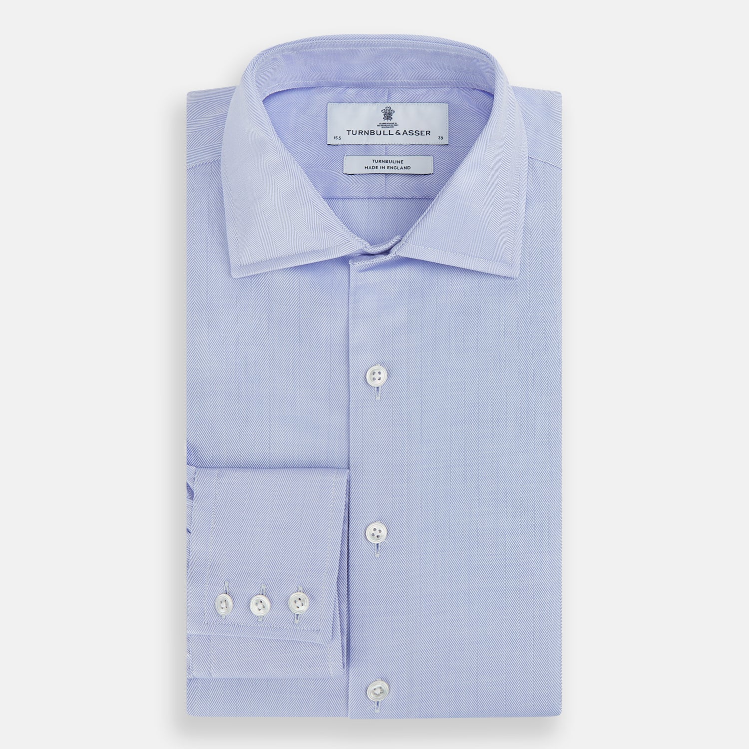 View 5 of product The Turnbull & Asser BLUE HERRINGBONE TAILORED FIT SHIRT WITH KENT COLLAR features long sleeves and buttoned cuffs, offering a timeless formal look in a classic light blue herringbone fabric, laid flat on a white background.