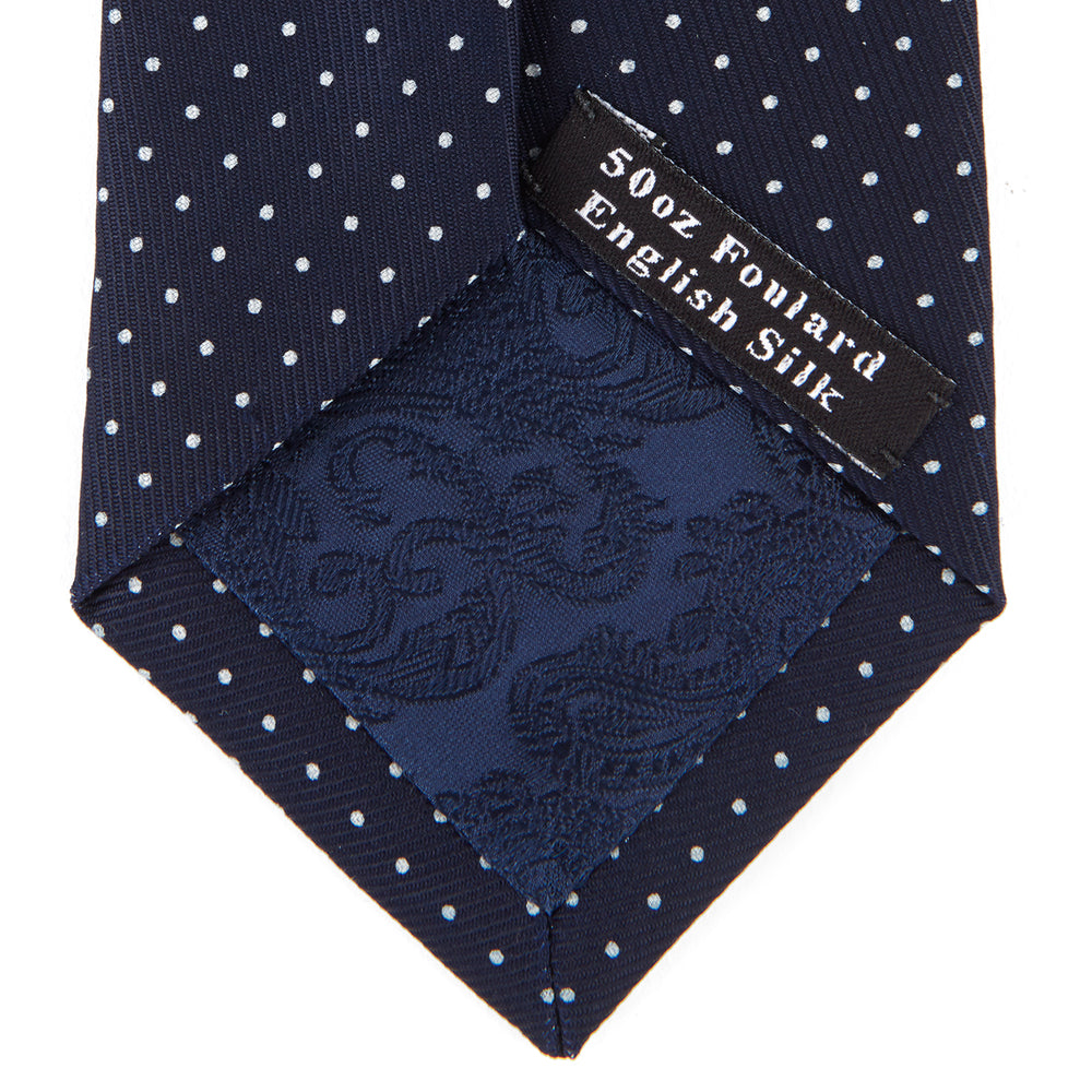 The Turnbull & Asser White and Navy Spot Printed Silk Tie, shown rolled with its pointed end forward on a white background, is an elegant accessory that pairs perfectly with a crisp shirt for smart occasions.