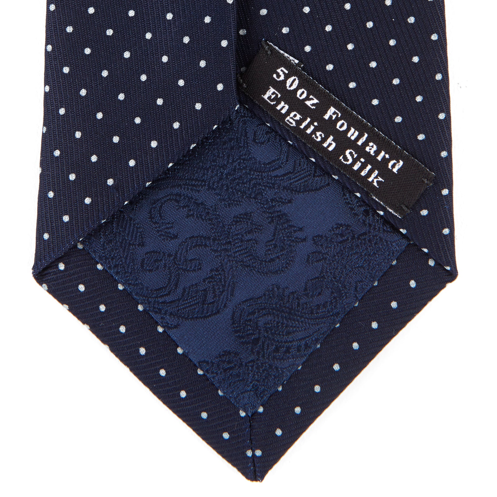 View 4 of product The Turnbull & Asser White and Navy Spot Printed Silk Tie, shown rolled with its pointed end forward on a white background, is an elegant accessory that pairs perfectly with a crisp shirt for smart occasions.