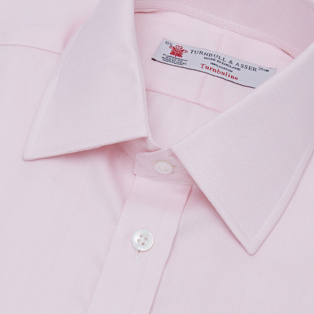 A Pink Herringbone Superfine Cotton Shirt by Turnbull & Asser, featuring a T&A collar and 3-button cuffs, is neatly folded with the inner collar label visible and white buttons, set against a plain white background.