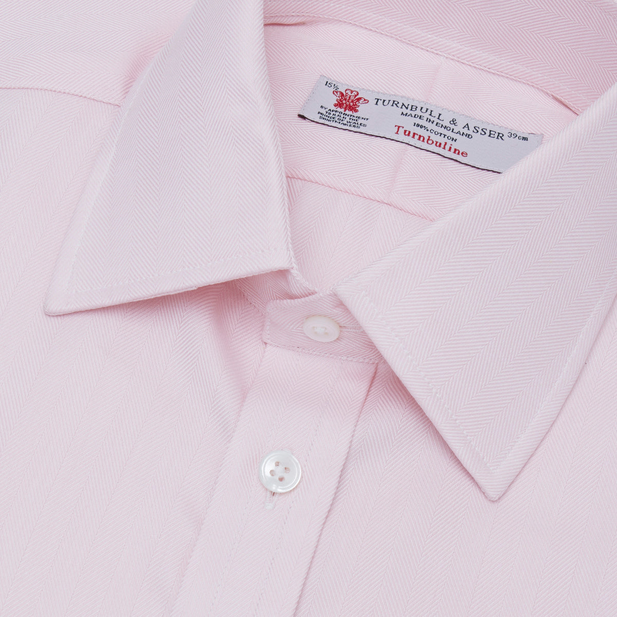 View 5 of product A Pink Herringbone Superfine Cotton Shirt by Turnbull & Asser, featuring a T&A collar and 3-button cuffs, is neatly folded with the inner collar label visible and white buttons, set against a plain white background.