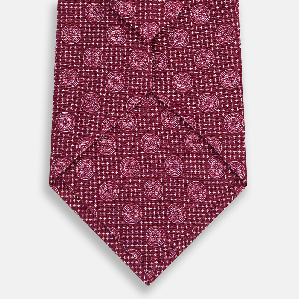 The Turnbull & Asser Burgundy Medallion Silk Tie features a geometric pattern of small circles intersected by diagonal pink lines, elegantly displayed against a white background.