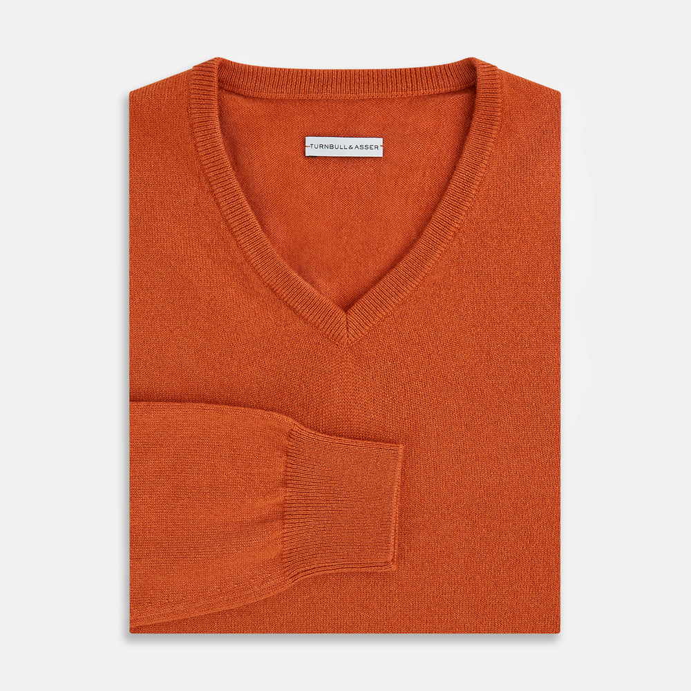 The Turnbull & Asser Rust Cashmere V-neck Jumper features long sleeves, ribbed cuffs and hem, and is shown against a plain white background.