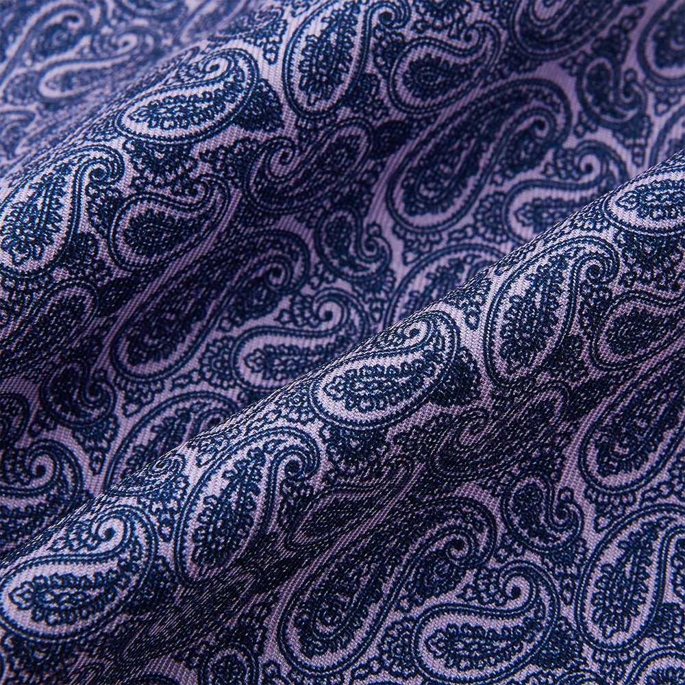 The Turnbull & Asser Lilac Paisley Silk Cravat showcases British elegance with its dark blue paisley pattern on a lilac background, beautifully displayed on a white surface.