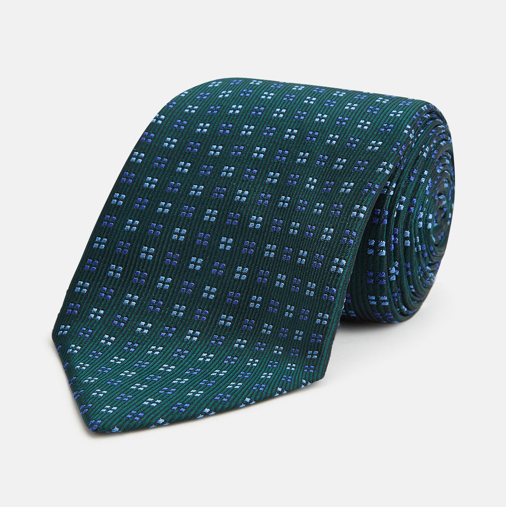 The MINI SQUARE SPOT FOREST GREEN BLUE TIE by Turnbull & Asser is a classic men's accessory, featuring a rolled-up green silk design with small blue geometric patterns—perfect for the modern gentleman.