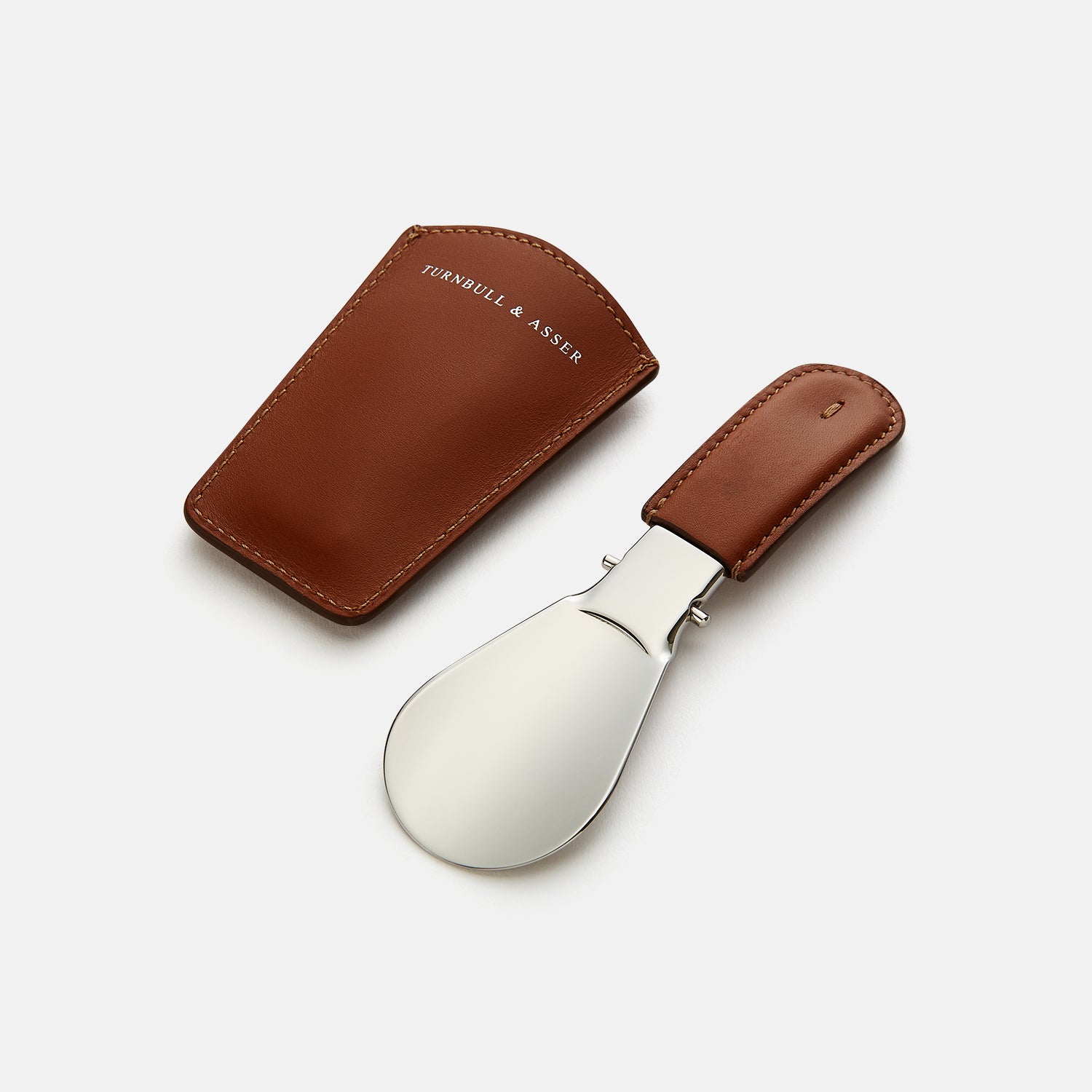 View 3 of product The Turnbull & Asser Camel Travel Shoe Horn features a wide, shiny silver blade and a brown Italian leather handle, displayed on a plain light background.