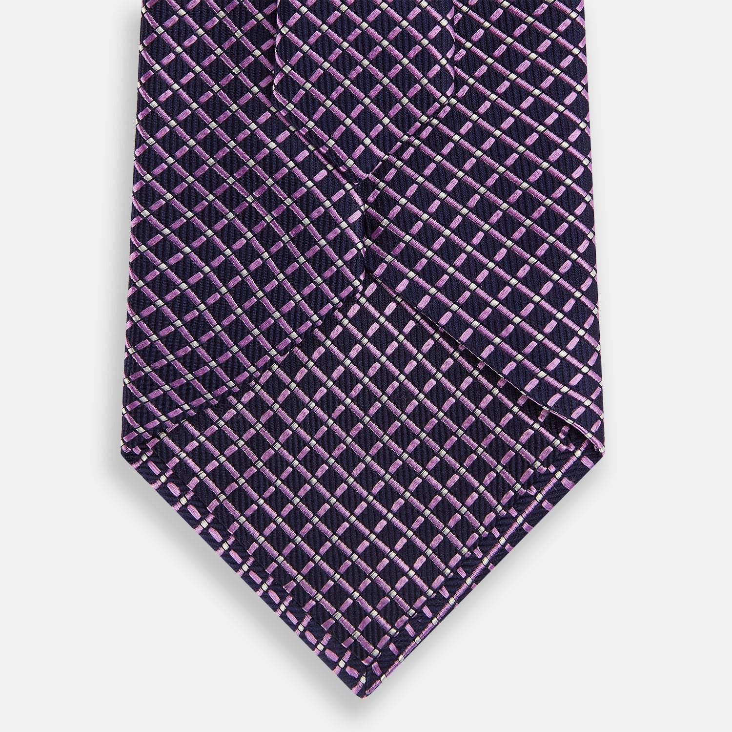 View 3 of product A rolled-up Turnbull & Asser Purple and Navy Diamond Silk Tie displays its elegant grid pattern of light pink and white lines on a white background.