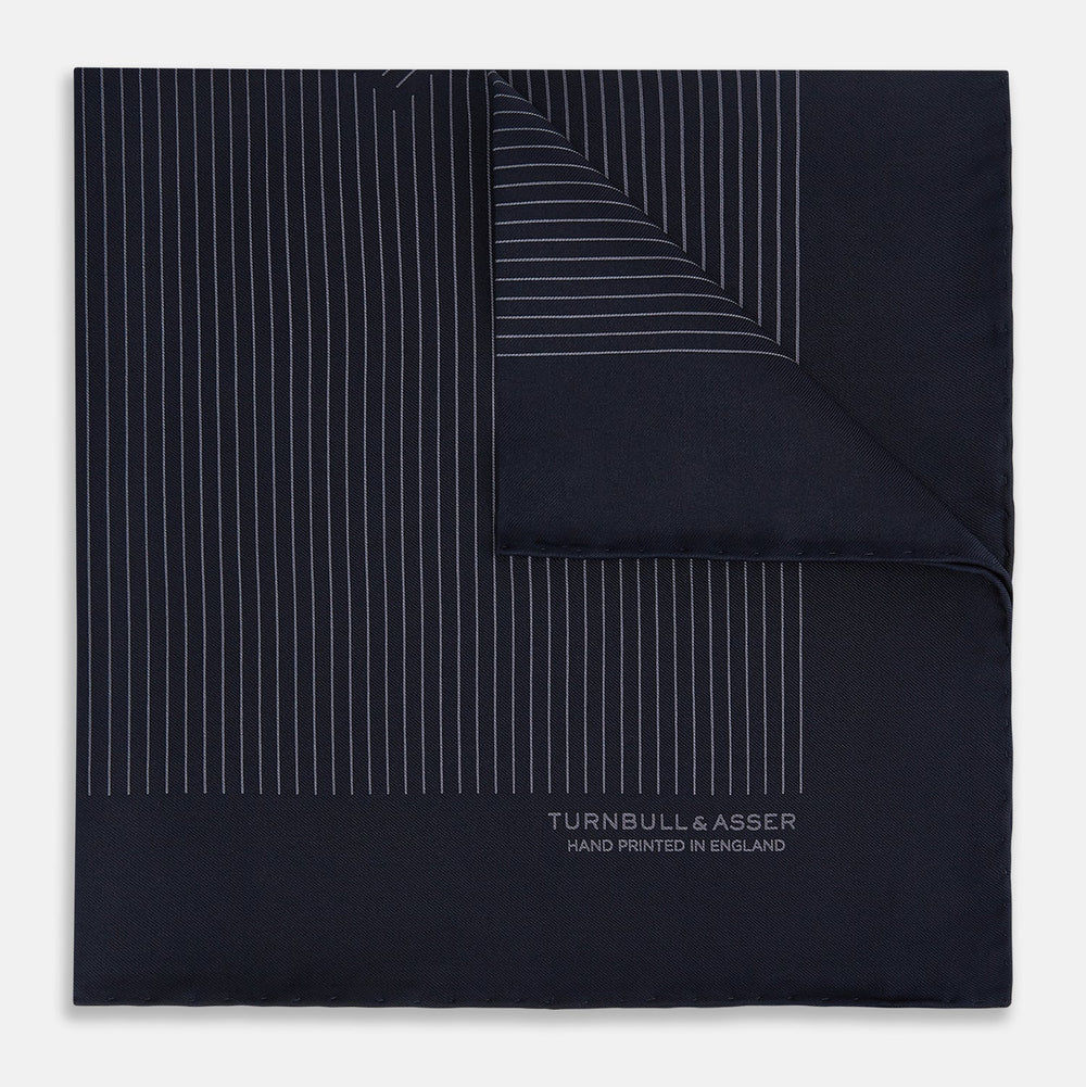 The Navy and Charcoal Stripe Silk Pocket Square by Turnbull & Asser features fine hand-rolled edges, thin white stripes on navy, and TURNBULL & ASSER HAND PRINTED IN ENGLAND in white on the corner.