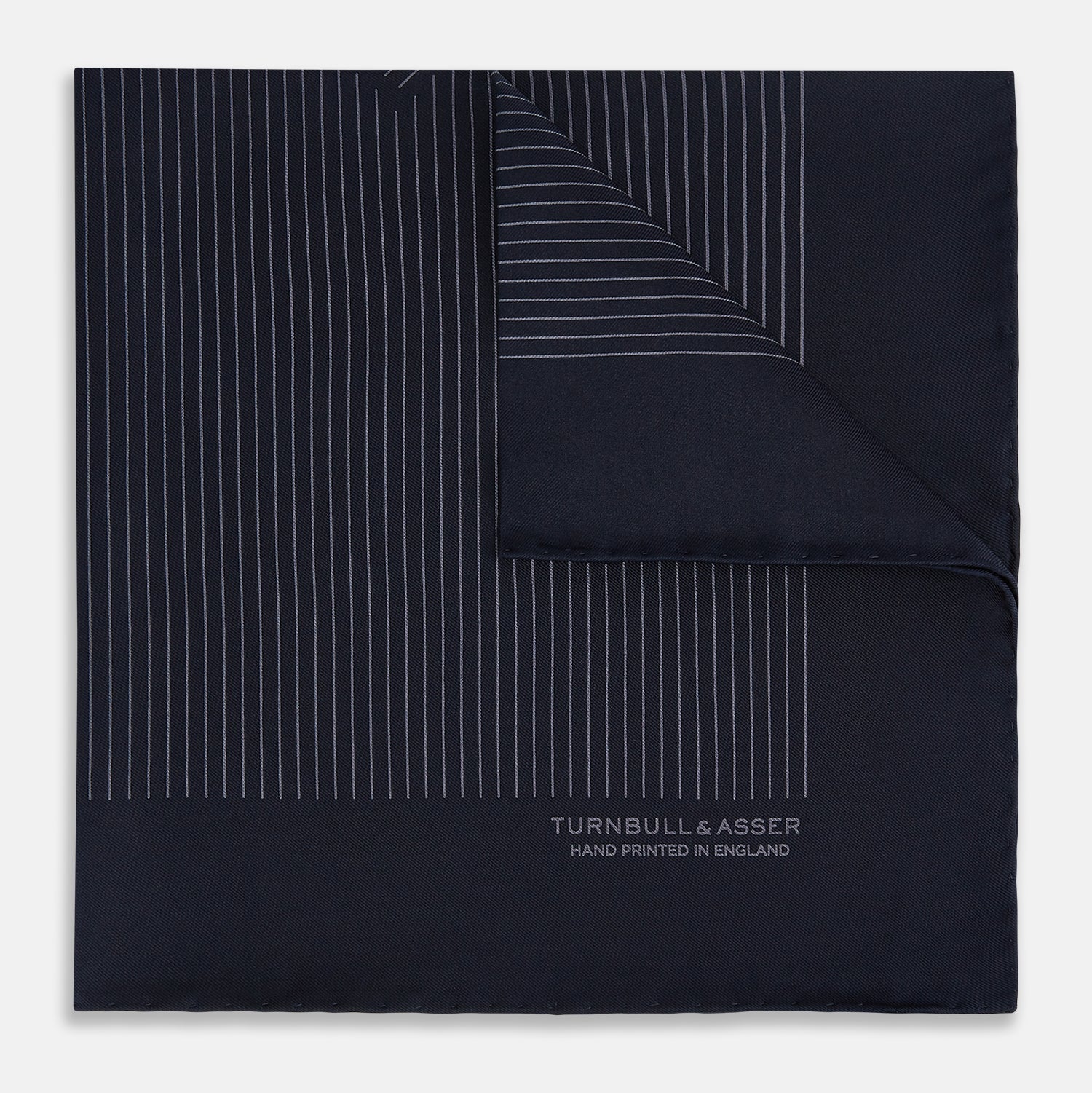 View 1 of product The Navy and Charcoal Stripe Silk Pocket Square by Turnbull & Asser features fine hand-rolled edges, thin white stripes on navy, and TURNBULL & ASSER HAND PRINTED IN ENGLAND in white on the corner.