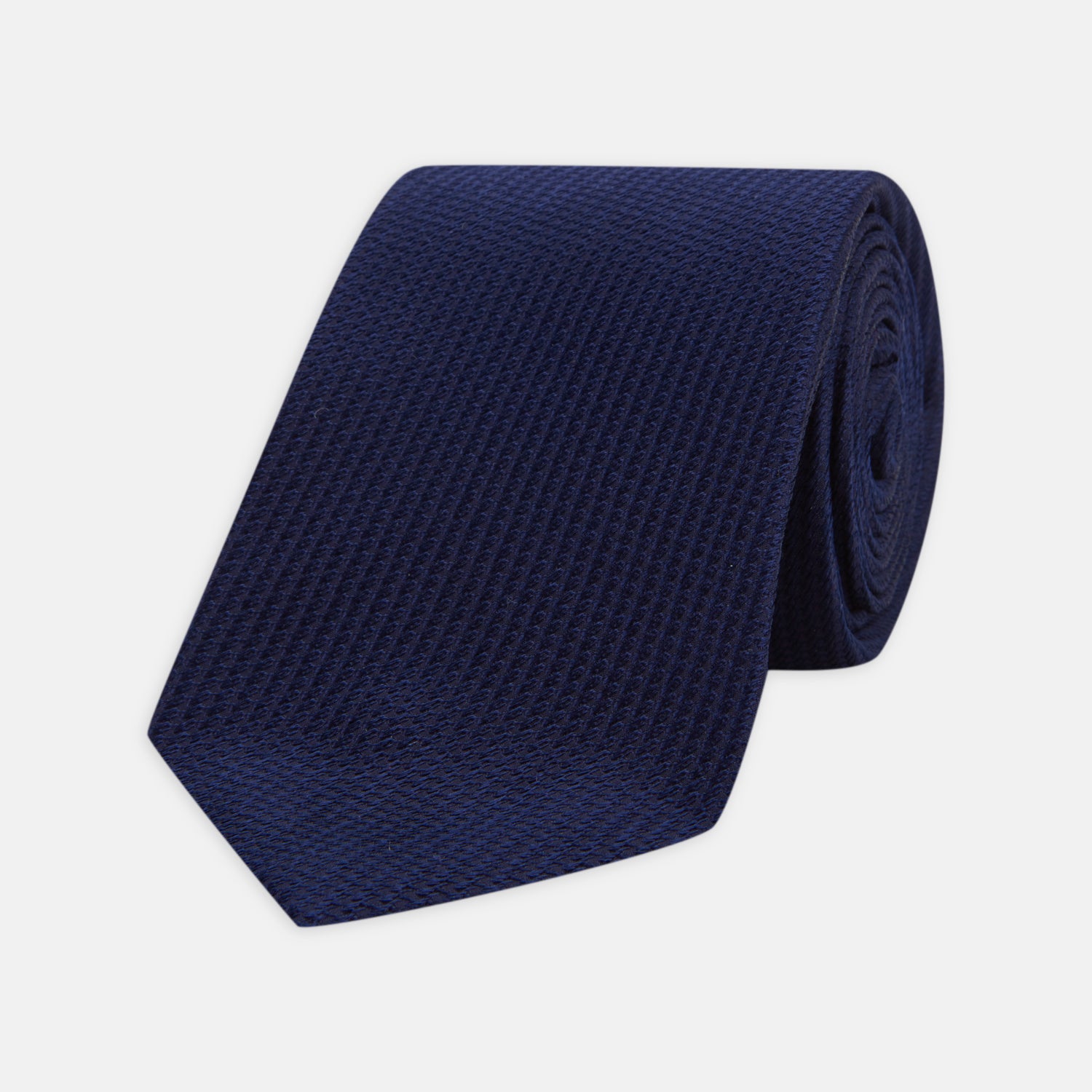 View 1 of product The Turnbull & Asser Seven-Fold Navy Lace Silk Tie is shown on a white background, rolled at one end with the pointed tip facing forward.