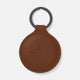A tan circular leather fob holder by Turnbull & Asser, featuring visible stitching, embossed branding, and 'Made in England,' attached to a metal key ring.