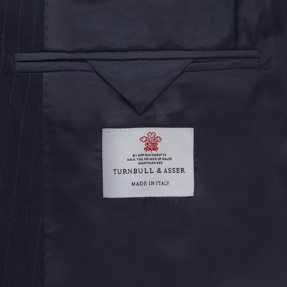 The Turnbull & Asser Navy Wool Pinstripe Double-Breasted Jacket features peak lapels, four front buttons, and three front pockets, and is displayed on a plain white background.