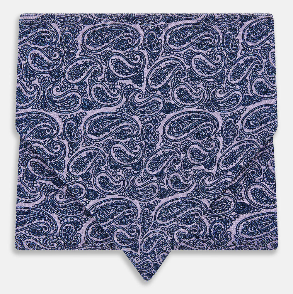 The Turnbull & Asser Lilac Paisley Silk Cravat showcases British elegance with its dark blue paisley pattern on a lilac background, beautifully displayed on a white surface.