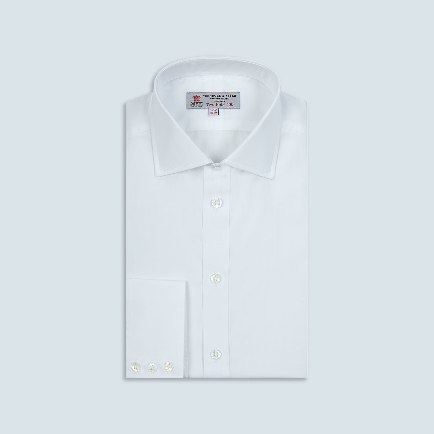 View 1 of product A neatly folded Turnbull & Asser Two-Fold 200 White Cotton Shirt with a Regent collar and 3-button cuffs, crafted from breathable fabric, is displayed on a light grey background with the label visible inside the collar.