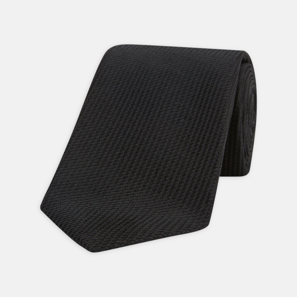 Turnbull & Asser's Seven-Fold Black Lace Silk Tie, featuring a textured finish and pointed tip, is elegantly rolled and displayed on a white background—a timeless accessory for any luxury neckwear collection.