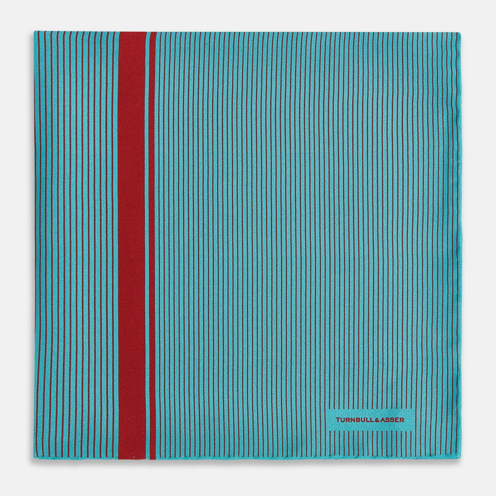 The Turnbull & Asser Turquoise and Red Stripe Silk Pocket Square features thin navy stripes with a bold vertical red stripe, partially folded to reveal the reverse pattern and the brand's logo, showcasing its British heritage.