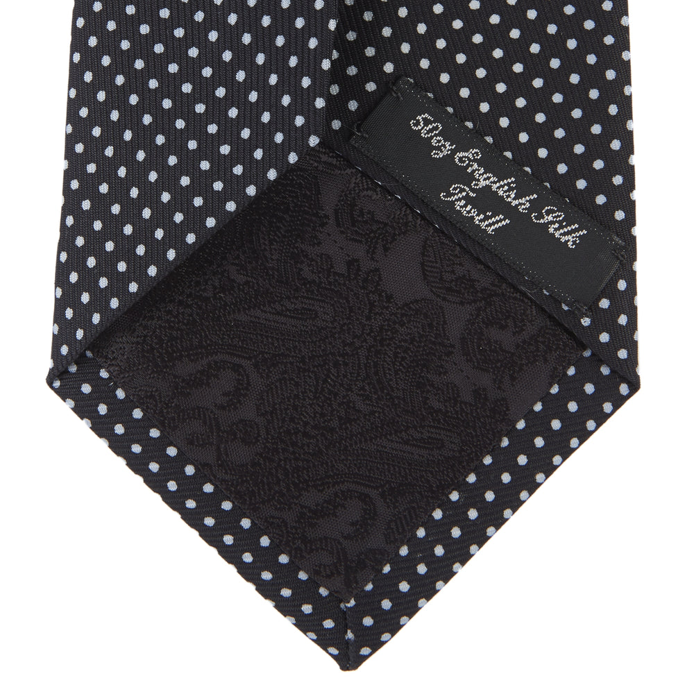The Turnbull & Asser Black and White Spot Printed Silk Tie, shown neatly rolled on a plain white background, is an essential accessory to elevate any smart attire.