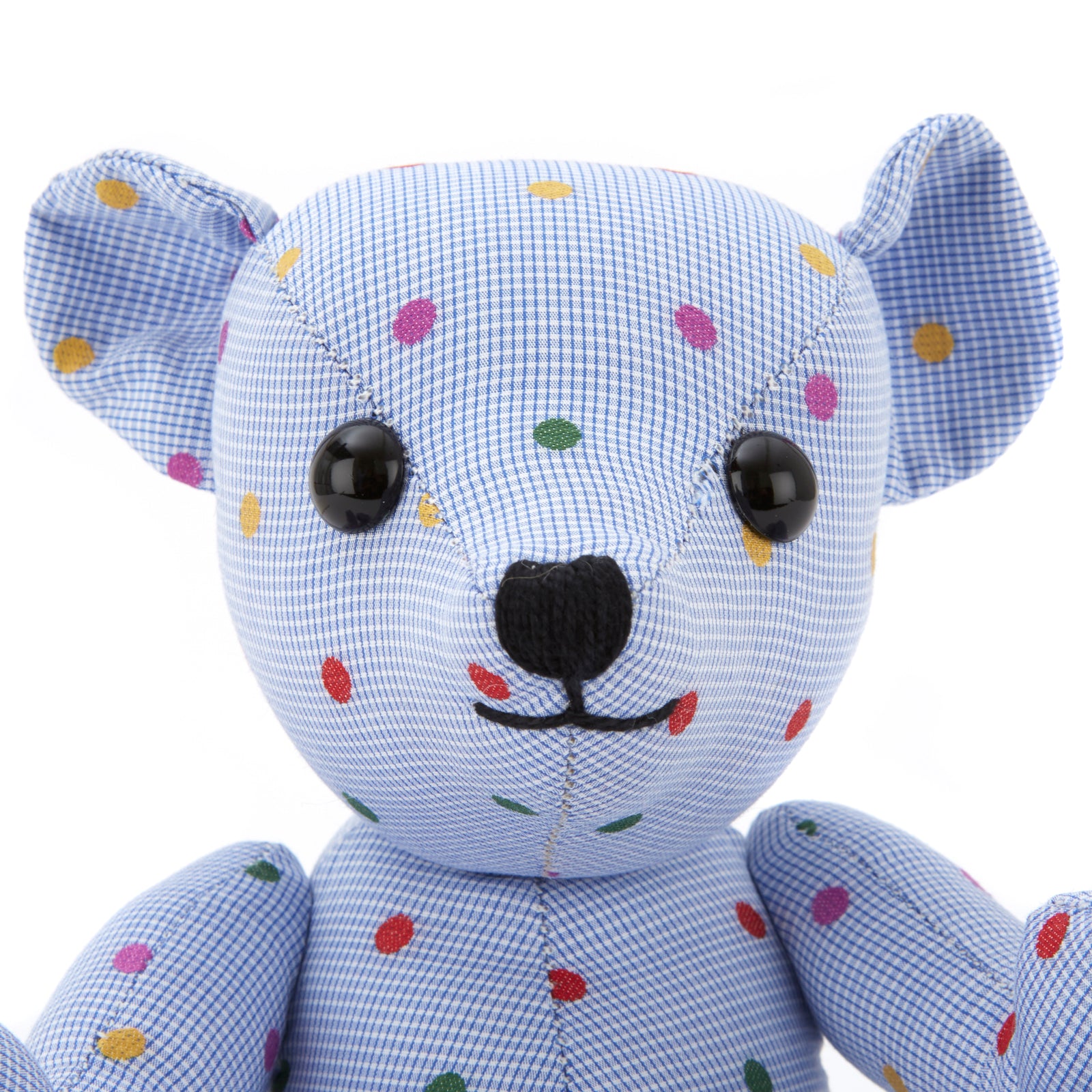 View 2 of product The Turnbuline Cotton Spot Teddy Bear by Turnbull & Asser is a blue gingham bear with colorful polka dots, black button eyes, a black nose, and a white leg label, shown sitting upright in profile facing left.