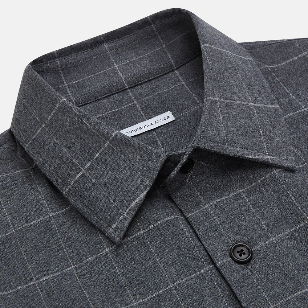 The Turnbull & Asser Charcoal Melange Check Hampstead overshirt, a long-sleeve button-up with a collar and two zippered side pockets, is laid flat on a light gray background.