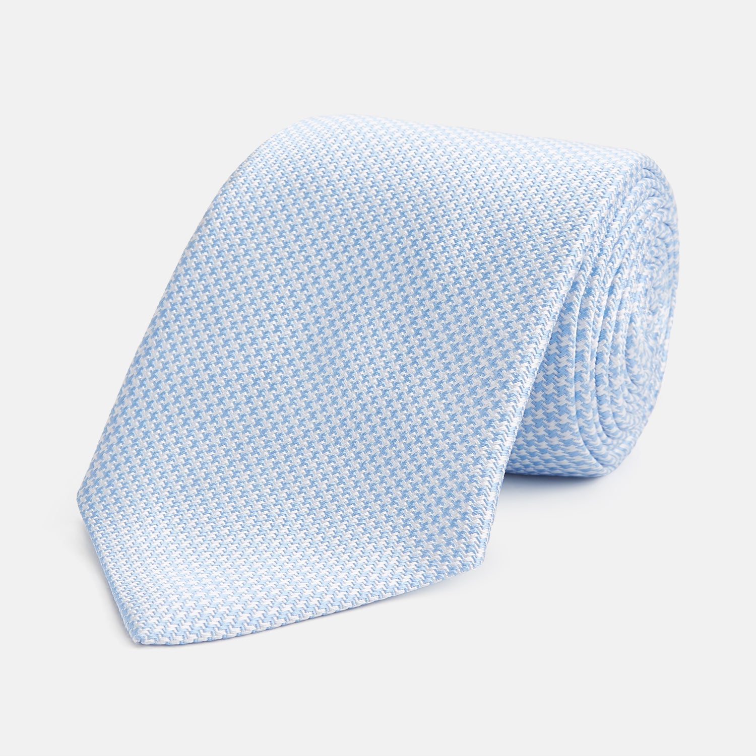 View 1 of product The HOUNDSTOOTH WHITE RIVER TIE by Turnbull & Asser features a light blue and white textured pattern, making it an essential accessory for elegant looks, shown beautifully rolled on a plain white background.