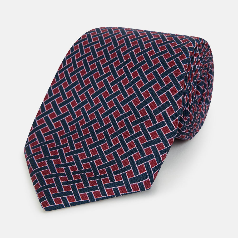 The Turnbull & Asser Navy and Pink Woven Printed Silk Tie features a geometric pattern with interlocking lines, displayed rolled on a light background—perfect for pairing with formal shirts.